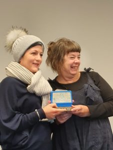 Two women posing with a trophy. One wearing an outstanding white bobble hat