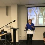 Woman at a lecturn in front of powerpoint presentation