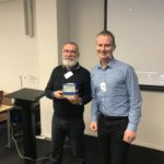 Two men smiling, one holding a plastic toaster