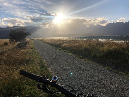 Sun going behind a stormy looking cloud over a lake with a straight gravel road beside it