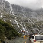 Line of cars waiting in traffic to enter Milford Sound alongside a massive rockface on the left