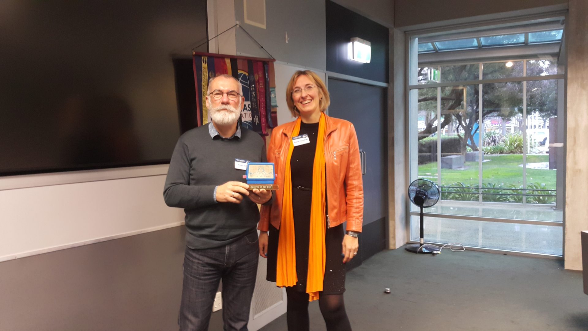 Toastmaster of the week receiving the Toastie award from another member, both smiling at the camera