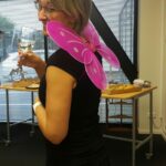 Woman wearing pink fairy wings standing side on to the camera looking over her shoulder, holding a glass of champagne