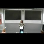 Screenshot of a hybrid meeting showing speaker in a lecture theatre and a thumbnail of the zoomer in the top right